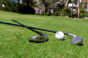 Golfschläger und Ball auf dem Rasen mit Gebäuden im Hintergrund