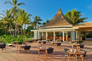 Außenterrasse des Kuramathi Maldives Hotels mit runden Tischen und Stühlen unter Palmen