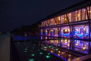 Nachtansicht des Kuramathi Maldives Hotels mit beleuchtetem Pool und Innenbereich.