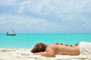 Eine Person genießt eine Massage auf dem Strand von Kuramathi Maldives mit einem Boot im Hintergrund.