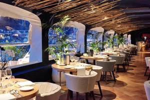 Innenbereich des Grand Hotel Poltu Quatu mit Restauranttischen und Pflanzen.