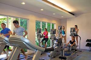 Fitnessraum im La Pirogue Mauritius Hotel mit mehreren Personen, die auf verschiedenen Trainingsgeräten trainieren.