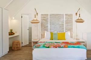 Schlafzimmer im La Pirogue Mauritius Hotel mit weißem Bett, farbigen Kissen und hängenden Lampen.