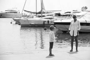 Schwarz-Weiß-Foto von einem Hafen mit mehreren weißen Booten und zwei Personen, einer Frau und einem Kind, die am Ufer stehen.