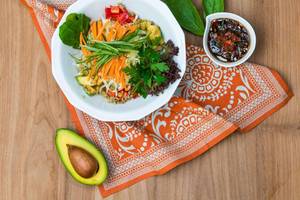 Teller mit Gemüsesalat und Avocado auf einem orangefarbenen Tuch