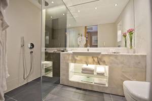 Das elegante Badezimmer des Akra Hotels mit einer großen Glasdusche und einem Marmorwaschtisch.