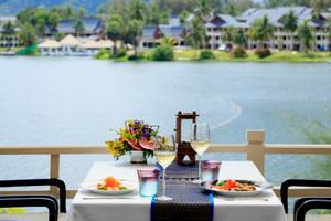 Terrasse im Dusit Thani Laguna Phuket mit einem Tisch, auf dem Essen, Wein und Dekor stehen.