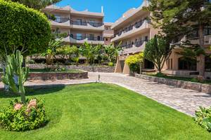 Außenbereich des Themis Beach Hotels mit gepflegtem Rasen, Gehweg und Gehölzen.