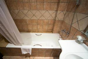 Ein Badezimmer mit einer Badewanne, einer weißen Dusche, braunen Fliesen und einem Spiegel.