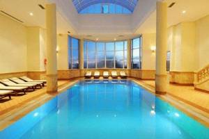 Indoorpool des Green Palm Hotels mit blauem Wasser und Sonnenliegen.