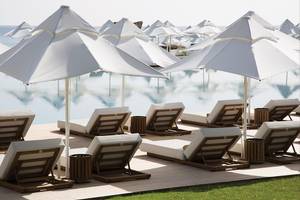 Außenbereich des Maxx Royal Kemer Resorts mit weißen Sonnenschirmen und Liegestühlen am Pool