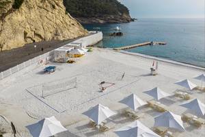 Strandvolleyballplatz am Maxx Royal Kemer Resort mit weißen Sonnenschirmen und Liegestühlen.