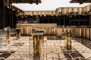 Ein eleganter Bereich im Maxx Royal Kemer Resort mit Glastischen, goldenen Säulen und einer Theke mit dem Wort Chocolatier.