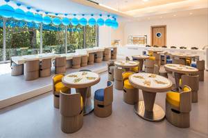 Innenbereich des Maxx Royal Kemer Resort mit mehreren Tischen und Stühlen, blauen Lichtern und großen Fenstern.