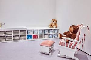 Ein kinderzimmer im Maxx Royal Kemer Resort mit einem weißen schaukelstuhl, einem hocker, truhen und teddybären.