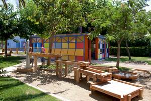 Kinderspielplatz im Freien mit bunten Gebäuden und Holzspielzeug im Sand.