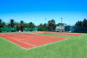 Tennisplätze im Freien im Aquila Rithymna Beach Hotel, umgeben von grünem Rasen und hohen Bäumen.