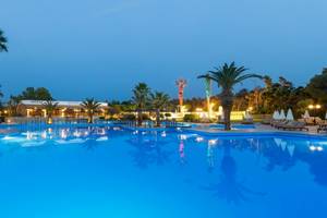 Pool des Aquila Rithymna Beach Hotels bei Nacht mit Palmen und Lounge-Sesseln