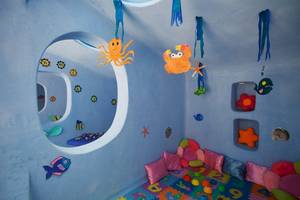 Unterwasserthematisches Kinderzimmer im Aquila Rithymna Beach Hotel mit blauen Wänden, Meerestieren und Spielzeug.