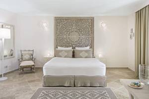 Innenansicht eines Schlafzimmers im Falkensteiner Resort Capo Boi mit großem Bett und kunstvollen Wanddekorationen.