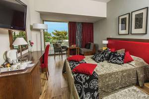 Schlafzimmeransicht im Kristall Springs Beach Hotel mit einem großen Bett, rotem Kopfteil und Blick auf den Balkon.