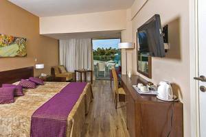 Innenansicht eines Zimmers im Crystal Springs Beach Hotel mit Bett, Fernseher und Balkon.