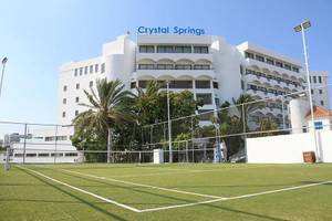 Außenansicht des Crystal Springs Beach Hotels mit Tennisplatz und Gebäude im Hintergrund.