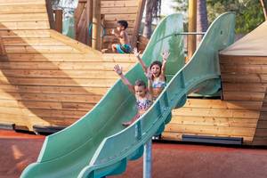 Kinder rutschen im Freizeitpark, zwei Mädchen und ein Junge im Hintergrund.