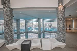 Innenpool-Ansicht im Vassos Nissi Plage Hotel mit weißen Sesseln und gefliesten Säulen.