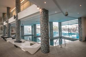 Pool-Loungebereich im Vassos Nissi Plage Hotel mit weißen Liegestühlen und gefliesten Säulen.