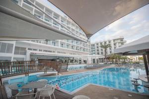 Poolbereich des Vassos Nissi Plage Hotels mit Liegestühlen und Gebäuden im Hintergrund.