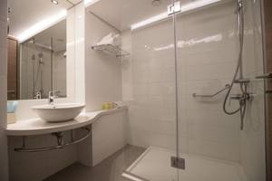 Ein modernes Badezimmer im Vassos Nissi Plage Hotel mit einer Dusche, Waschbecken und Handtüchern.