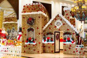 Ein Lebkuchenhaus in der Lobby des Jumeirah Zabeel Saray, geschmückt mit roten Blumen und Weihnachtsdekoration.