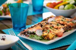 Gegrillter Garnelenteller mit Gemüse und Getränken auf einem Tisch serviert.
