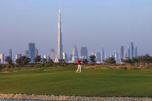 Golfplatz mit einem Spieler im Vordergrund und der Skyline von Dubai im Hintergrund.