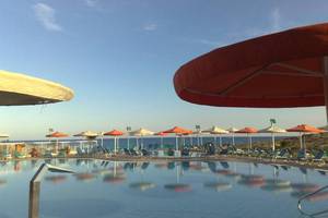 Außenpool des Aktea Beach Village Hotels mit Sonnenschirmen und Liegestühlen am Meer
