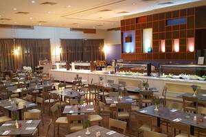 Innenansicht des Restaurants im Aktea Beach Village Hotel mit vielen gedeckten Tischen und einer langen Theke im Hintergrund.