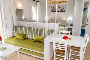 Aktea Beach Village Zimmer mit grünem Sofa, Tisch und Stühle, weißer Wand und Fenster.