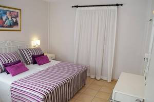 Ein modernes Schlafzimmer im Aktea Beach Village Hotel mit einem Doppelbett, farbigen Kissen und weißen Vorhängen.