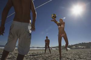 Volleyball-Spieler auf dem Strand mit der Sonne im Hintergrund.