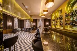 Bar-Inneneinrichtung des Ancient Sands Golf Resorts mit gemustertem Boden, Sesseln und einer Theke mit Silberschüssel.