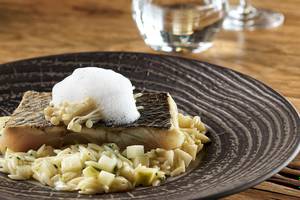 Fischgericht mit Reis und Gemüse auf einem schwarzen Teller auf einem Holztisch.