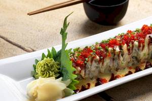 Eine Sushi-Rolle mit roter Kaviar- und Sojasaucen-Belag auf einem weißen Teller.