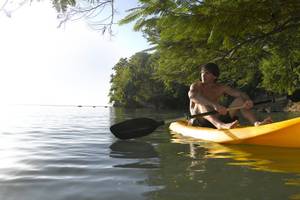 Ein Mann ohne Oberteil paddelt in einem gelben Kajak auf dem Wasser.