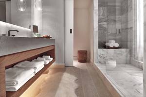 Innenansicht des Badezimmers im 1 Hotel South Beach mit Marmorfliesen, Glasdusche und Holzmöbeln.