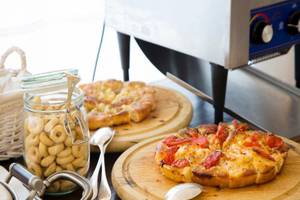 Tisch mit zwei Pizzen, einer Glasflasche mit Gebaecken und verschiedenen Essgeschirr auf dem Tisch