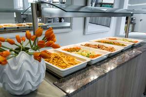 Buffettisch im Acharavi Beach Hotel mit verschiedenen Speisen und orangefarbenen Tulpen in einer weißen Vase.