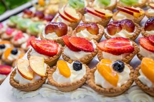 Nahaufnahme von Obsttartes auf einem Tisch, mit verschiedenen Früchten wie Erdbeeren, Äpfeln und Pflaumen.