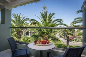 Balkon des Acharavi Beach Hotel mit Obstplatte und Aussicht auf Palmen und Straße.