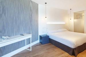 Ein elegantes Hotelzimmer im HM Gran Fiesta mit einem Bett, Nachttisch, Schreibtisch und modernen Lampen.